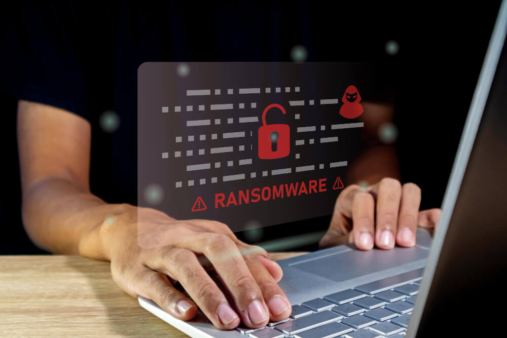 Ransomware in Mexico | Applivery Laptop user typing with a translucent overlay showing a ransomware warning: red padlock icon and warning symbols emphasizing a cyber threat.
