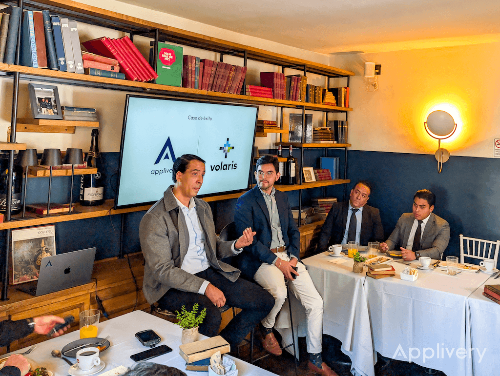 Panel discussion in a cozy library-like room with four men at a long table; screen shows Applivery and Volaris logos in the background.